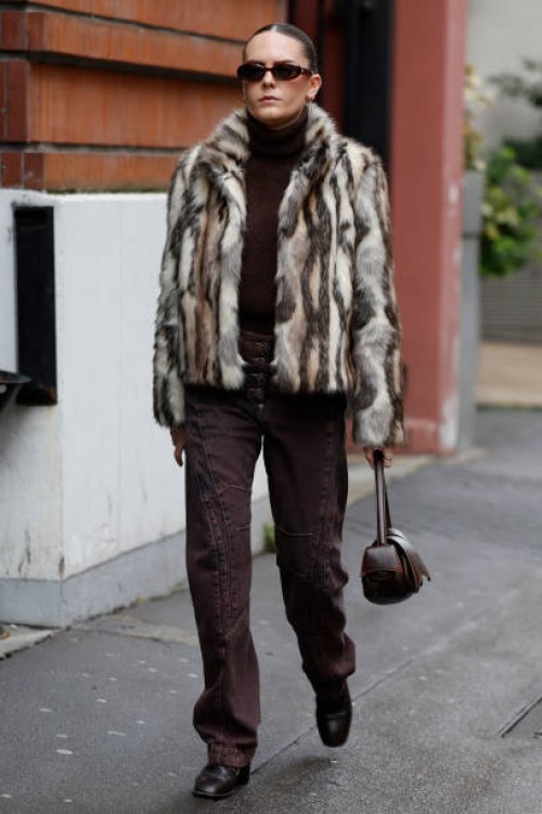 Guest wears brown turtleneck sweater, brown jeans, beige and brown fur jacket, brown bag, outside Kiko Kostadinov, during the Menswear Fall Winter...