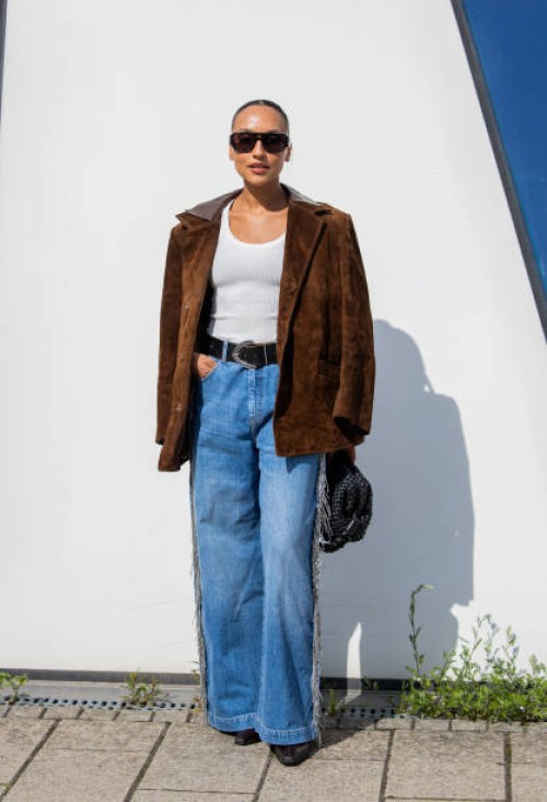 Guest wears brown wild leather jacket, black bag, denim jeans outside Munthe during day four of the Copenhagen Fashion Week SS25 on August 08, 2024...