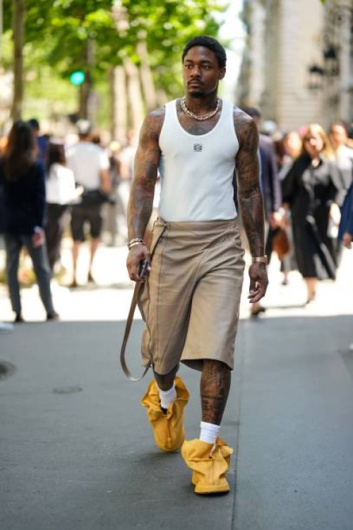 Guest wears cross pendant silver earrings, silver rhinestones necklaces, a white tank-top from Loewe, brown wrap shiny leather knees shorts, a gold...