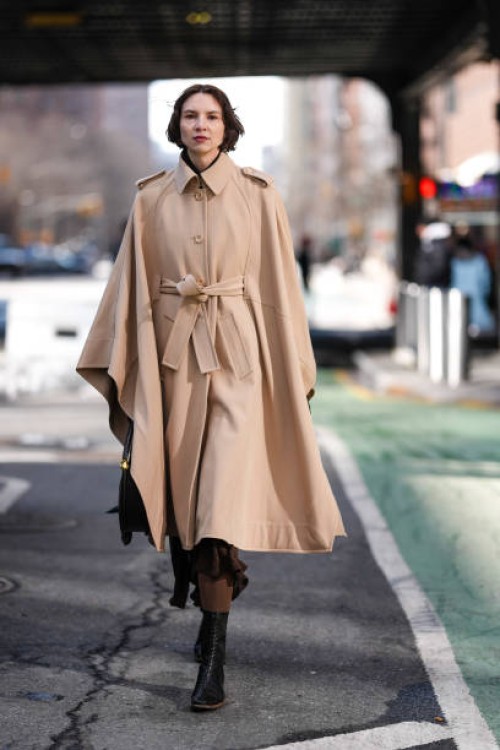 Guest wears dark brow belted trench cape, dark brown midi skirt, dark brown tights, shiny black pointed toe heel leather shoes, shiny black leather...
