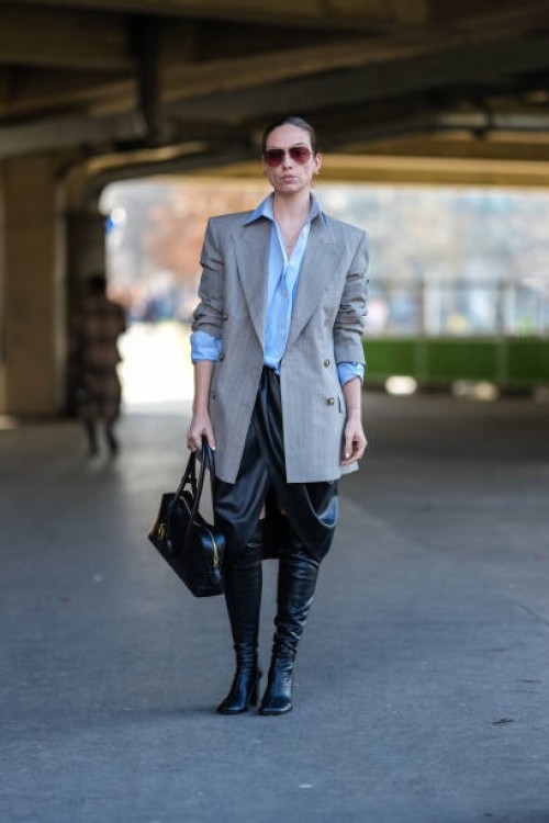 Guest wears dark brown aviator sunglasses, gold earrings, light blue oversized half buttoned long sleeve shirt, light gray white pinstripe double...