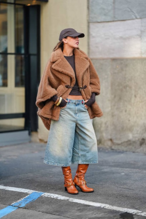 Guest wears dark brown Baseball hat, dark brown long sleeve shirt, light brown teddy bear oversized Max Mara coat, washed denim jean jorts, light...