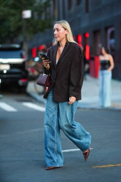 Guest wears dark brown oversized blazer jacket, dark brown Tory Burch leather handbag, gold rings, gold bracelets, washed light blue denim jean...