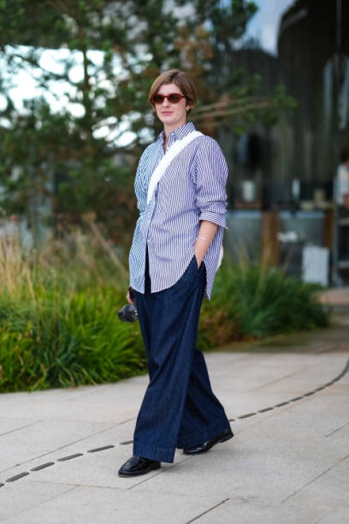Guest wears dark brown sunglasses, light blue white lined button up long sleeve shirt, silver bracelet, white leather bag, navy blue denim jean...