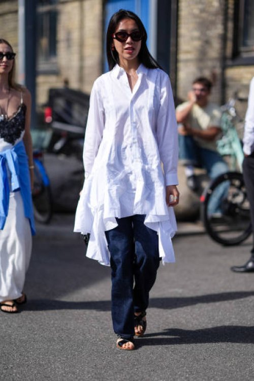 Guest wears dark brown sunglasses, white Comme Des Garcons button up long sleeve shirt dress with ruffled layered bottom, silver rings, navy dark...