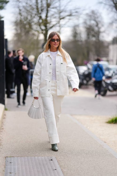 Guest wears dark brown sunglasses, white t-shirt, gold layered necklaces, cream oversized denim jean Lacoste jacket, cream loose denim jean cuffed...