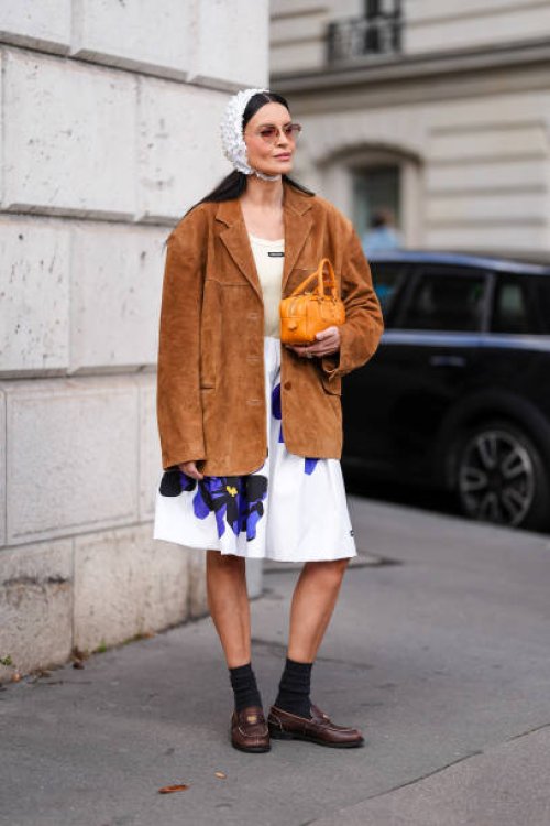 Guest wears dark brown sunglasses, white textured cap, dark brown suede oversized Miu Miu blazer jacket, cream tank top, white loose purple floral...