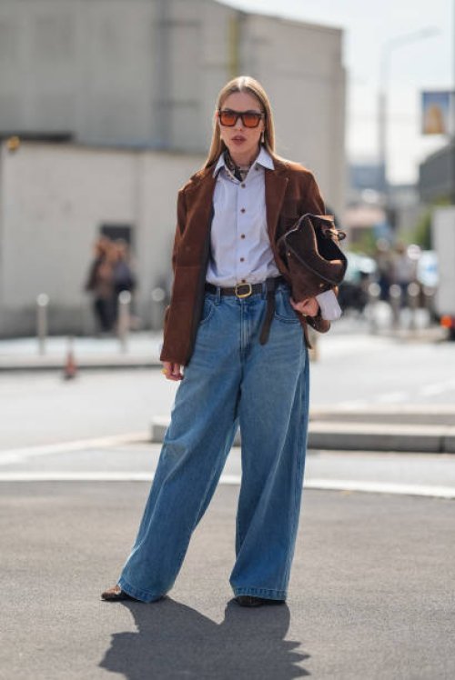 Guest wears dark brown sunglasses with orange lenses, light blue buttoned up long sleeve shirt, dark brown blazer jacket, dark brown leather belt,...