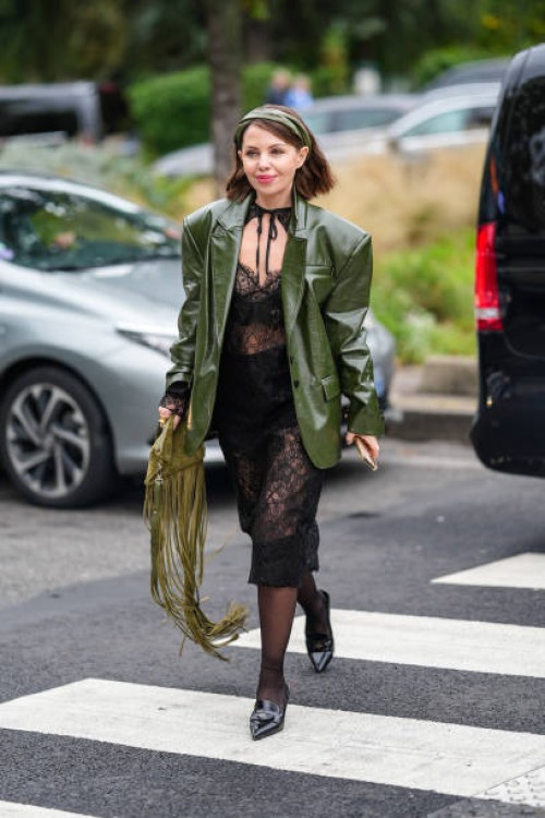 Guest wears dark green olive headband, shiny dark green olive oversized blazer jacket, black sheer mesh lace midi dress, dark green tassel bag, black...
