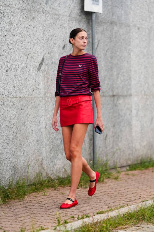 Guest wears dark red striped long sleeve shirt, black leather bag, bright red belted mini skirt, bright red ballerina flats, outside Jil Sander,...
