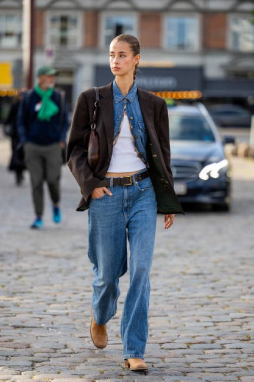 Guest wears denim jeans, shirt, brown oversized blazer outside Ganni during the Copenhagen Fashion Week Spring/Summer 2024 on August 10, 2023 in...