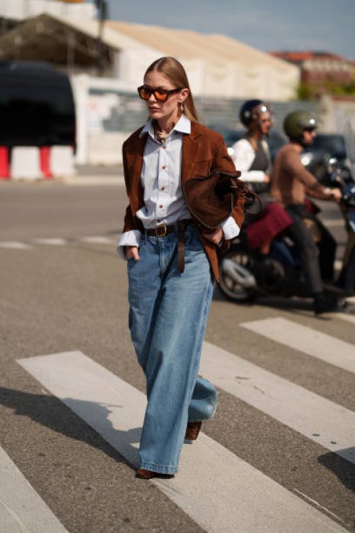 Guest wears denim wide leg jeans, a brown jacket, a bag, a blue button shirt is seen outside Prada show during the Milan Fashion Week Menswear...