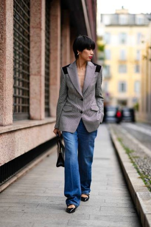 Guest wears earrings, a black and white houndstooth pattern oversized blazer jacket, a black crocodile pattern leather bag, blue denim jeans / pants,...