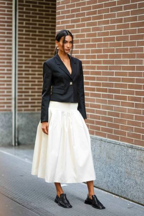 Guest wears earrings, a black Spencer jacket, a white gathered midi skirt, black leather moccasins, outside Fendi, during the Milan Fashion Week -...