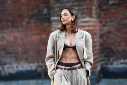 Guest wears earrings, a gray / beige full look, black bras and underwear, an opened oversized blazer jacket, a brown leather thin belt, flared pants...