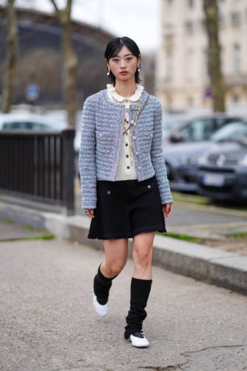 Guest wears earrings, a white pullover with ruffled collar, a pastel pale striped tweed jacket , a black mini skirt , knee high socks, white shoes,...
