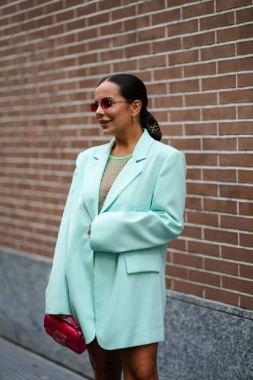 Guest wears Fendi sunglasses, earrings, a green fishnet top, an oversized light green jacket, a red leather Fendi bag , outside Fendi, during the...