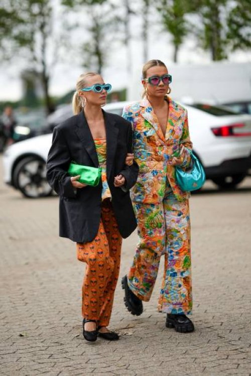 Guest wears flashy blue sunglasses, silver large earrings, a gold small necklace, a black oversized blazer jacket, a green shiny leather clutch, a...