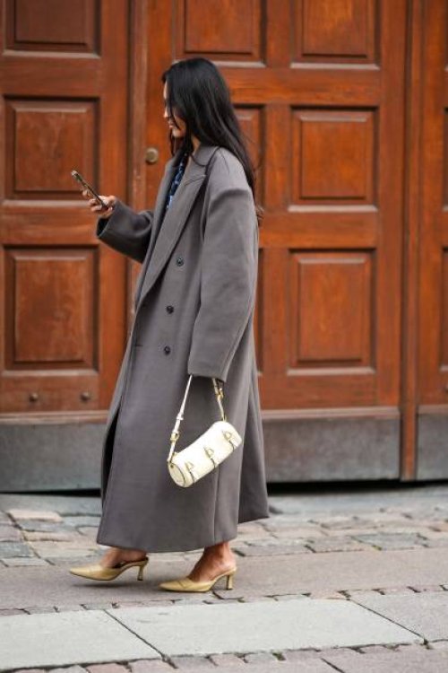 Guest wears gold earrings, a black and blue print pattern V-neck short dress, a gray oversized long coat, a white latte leather handbag, beige shiny...