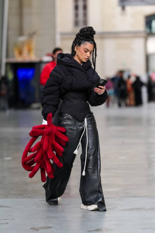 Guest wears gold earrings, black tailored puffer jacket, shiny black wide leg leather pants, dark red 3D graphic bag, white sneaker shoes, outside...
