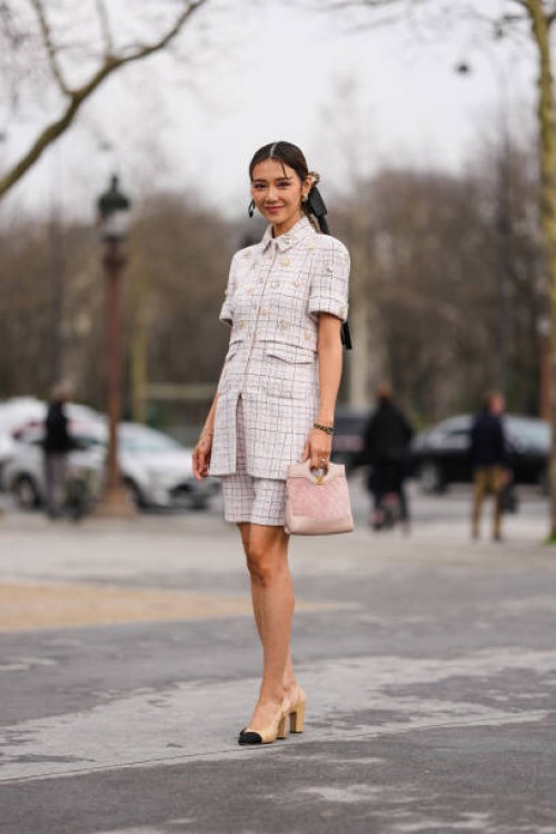 Guest wears gold earrings, dark brown braided hair with black bow, light pink pattern/print short sleeve buttoned light pink embellished Chanel...