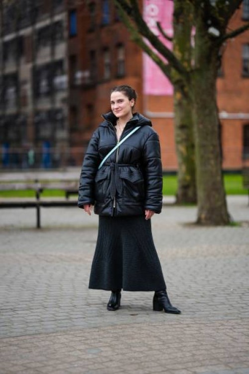 Guest wears gold earrings, gold long pendant earrings, a black shiny leather hoodie / belted coat, a pale blue shiny leather crossbody bag, a black...