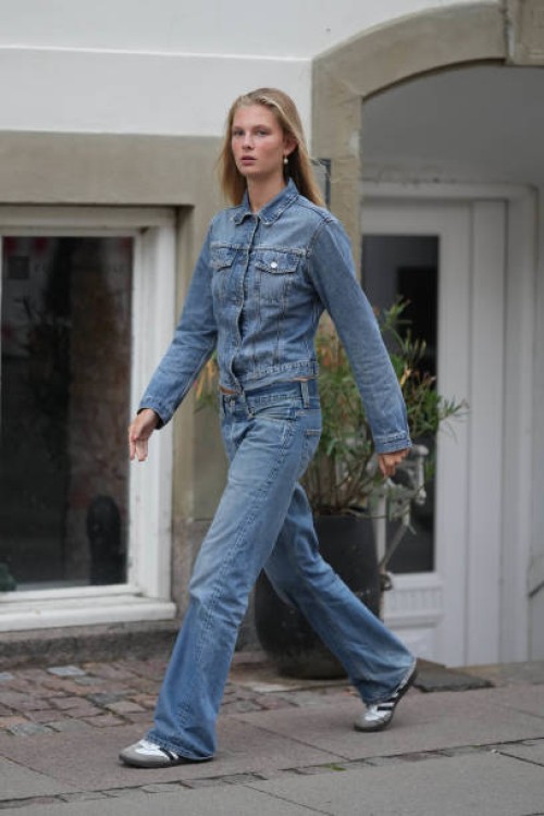 Guest wears gold with white pearl pendant earrings, a blue denim jacket, matching blue denim wide legs pants, white leather / gray suede / black logo...