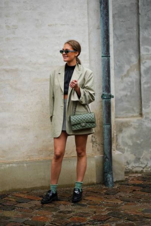 Guest wears gray sunglasses, blue stones earrings, a black high neck cropped silk top, a pale green oversized blazer jacket, a pale gray short skirt,...