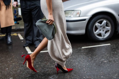 Guest wears grey green blue clutch, red heels, grey dress outside JW Anderson during London Fashion Week February 2024 on February 18, 2024 in...