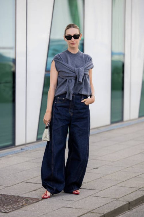Guest wears grey sleeveless knit, dark denim jeans outside Munthe during day four of the Copenhagen Fashion Week SS25 on August 08, 2024 in...