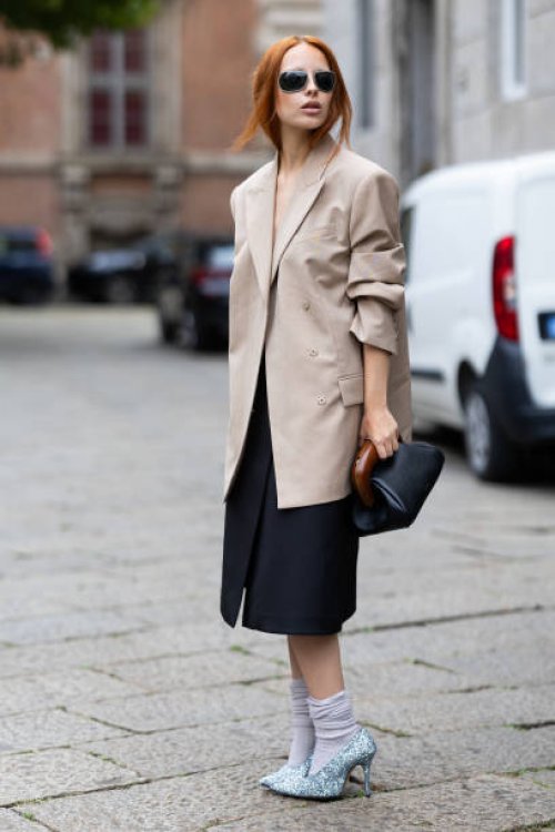 Guest wears grey socks, silver sparkly pumps, grey sunglasses, a beige blazer, a grey long skirt and a black lather bag outside Sportmax show during...