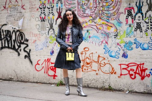Guest wears hair pins with pearl details, a silver necklace, a grey and purple crop top with prints and yellow striped details / tie and dye, a black...