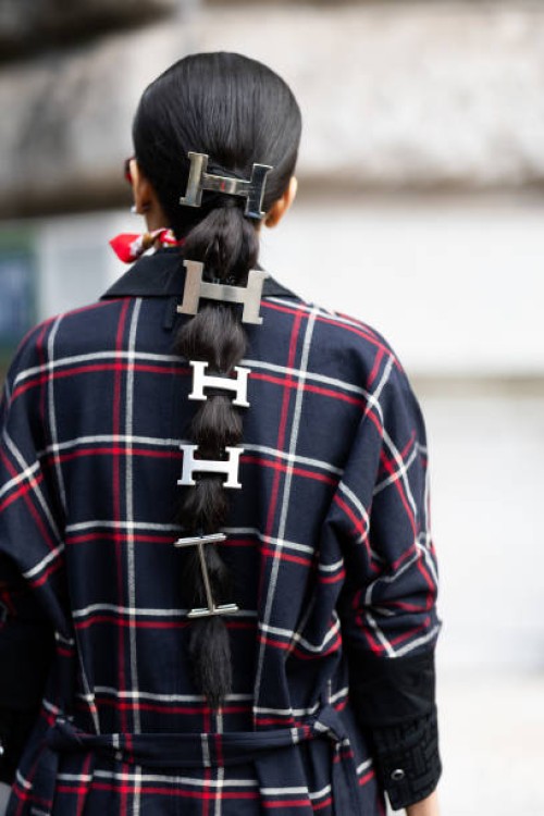 Guest wears Hermes silver hair accessories and a blue, red and white checked coat outside Hermes show during Womenswear Spring/Summer 2025 as part of...