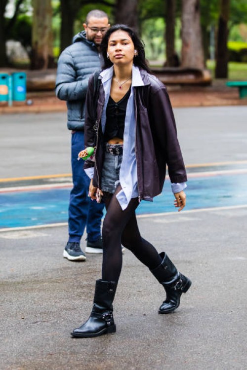 Guest wears leather jacket, black top, light blue button-up shirt underneath, denim shorts, black tights, black biker boots, belt with silver details...