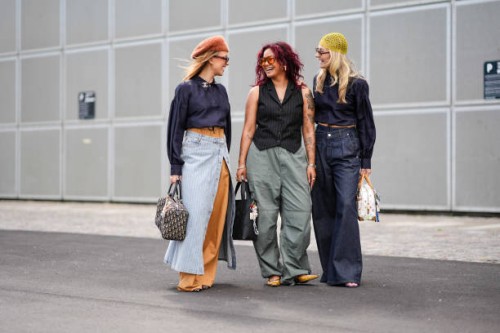 Guest wears light brown fuzzy hat, black sunglasses, black long sleeve cropped shirt with a Chanel pendant, light brown maxi skirt, light gray white...