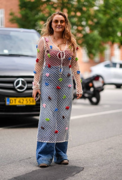 Guest wears light brown sunglasses, gold chain necklace with gold heart pendants, white sheer mesh long sleeve midi dress with red brown blue green...