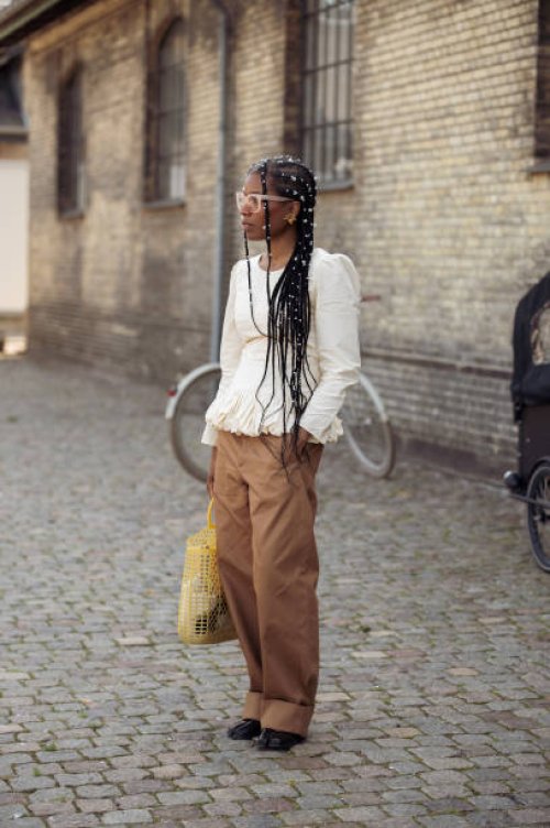 Guest wears light cream white shirt and brown pants, yellow bag and pearls as hair accessories outside the Herskind show during day three of the...