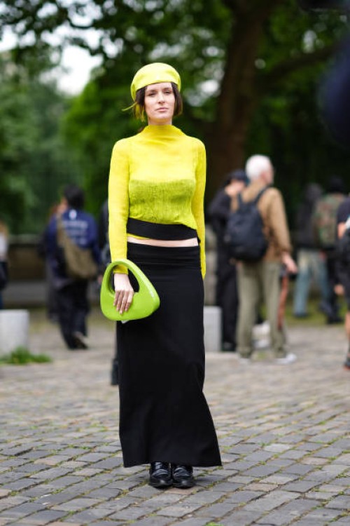 Guest wears lime bright green beret, lime bright green sheer mesh long sleeve top, strapless black top, lime green bag, low-waisted black maxi skirt,...