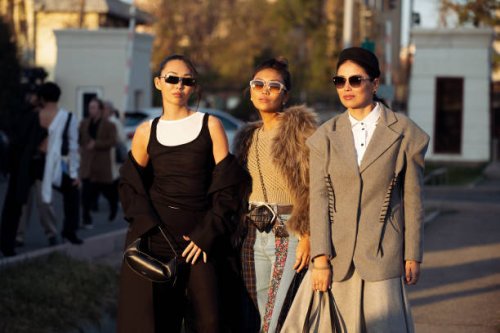 Guest wears long black skirt, white top, black top and black coat and a guest wears wide jeans, beige top and fur jacket and a guest wears grey long...