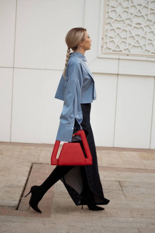Guest wears long denim maxi skirt with a split, light blue shirt and red bag during the Tashkent Fashion Week 2023 on November 28, 2023 in Tashkent,...