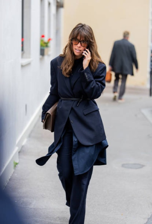 Guest wears navy belted blazer, pants, brown bag outside Gabriela Hearst during Womenswear Spring/Summer 2025 as part of Paris Fashion Week on...