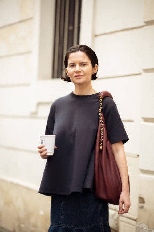 Guest wears navy blue T-shirt, dark blue denim skirt, burgundy bag outside the Loewe presentation during the Womenswear Fall/Winter 2025/2026 as part...