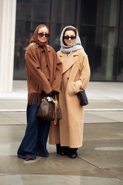 Guest wears navy blue wide pants, brown short coat with tassels and brown head scarf and a guest wears long beige coat, balck bag and grey balaclava...