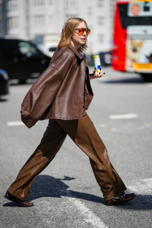 Guest wears orange sunglasses, a dark brown shiny leather oversized jacket, dark brown shiny leather large pants, dark brown shiny leather loafers ,...