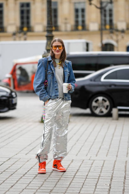 Guest wears orange sunglasses, a gray wool pullover, a blue denim jacket, a white with purple / orange / green print pattern shoulder bag from...