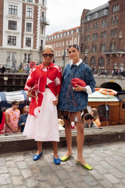 Guest wears pale pink skirt, blue ballerina shoes, red and pink pattern coat and red bag and a guest wears brown mini skirt, blue denim shirt, red...