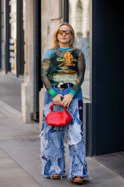 Guest wears patched denim jeans, red bag, shirt with graphic print outside Bora Aksu during London Fashion Week September 2024 on September 13, 2024...