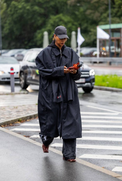 Guest wears rain coat, cap outside Saks Potts during the Copenhagen Fashion Week Spring/Summer 2024 on August 07, 2023 in Copenhagen, Denmark.
