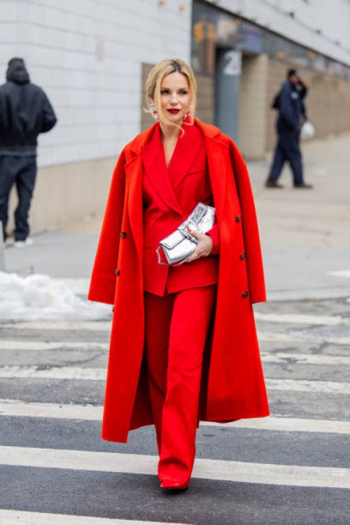 Guest wears red coat, blazer, pants, silver bag outside Michael Kors during New York Fashion Week on February 11, 2025 in New York City.