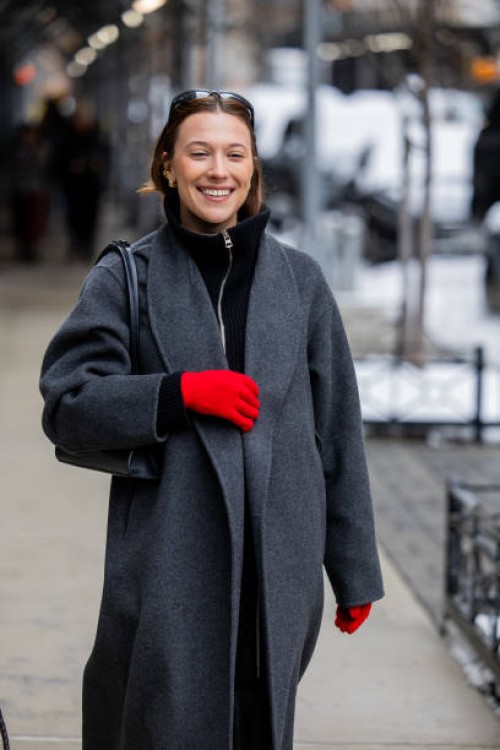 Guest wears red gloves, grey coat outside Ulla Johnson during New York Fashion Week on February 09, 2025 in New York City.